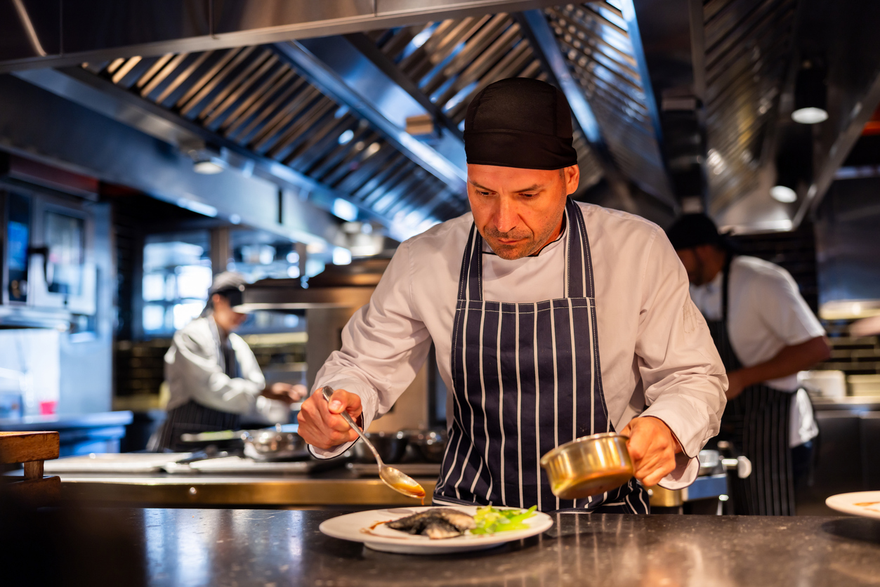 A chef finishing a dish with sauce in a professional kitchen
